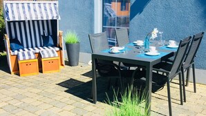 Eine Terrassengaststätte mit Esstisch, Stühlen, einer gestreiften Lounge und Topfpflanzen.