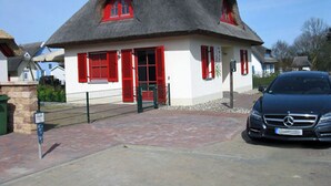 Una casa con techo de paja, contraventanas rojas y un coche estacionado adelante.