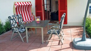 Un patio exterior con una mesa y sillas, un toldo a rayas y contraventanas rojas.