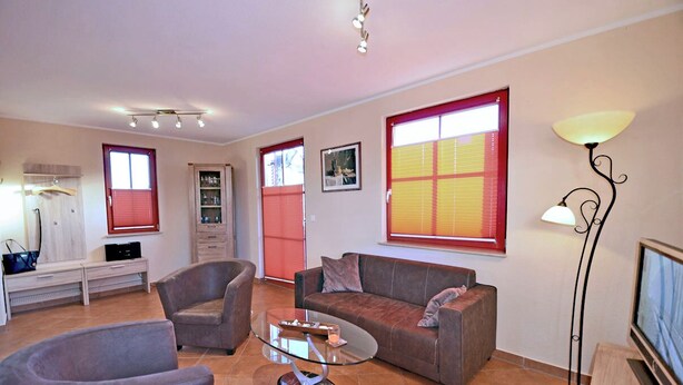 Una sala de estar con sofá, sillones, una mesa de centro, televisor y lámpara de pie.