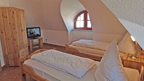 Un dormitorio con dos camas, un armario de madera, un televisor y una ventana con marco rojo.
