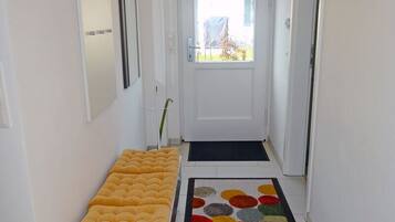 Um corredor com um banco, um tapete colorido e uma porta que dá para uma área externa.