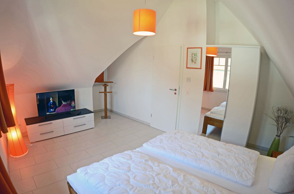 Een slaapkamer met een bed, televisie, kapstok en een deur naar een andere kamer.