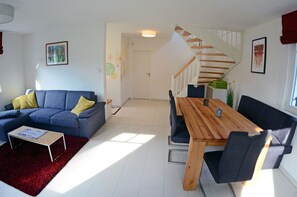 A modern living room with a blue sofa, a wooden dining table, and a staircase. - Vacation home with a fireplace, about 450 meters from the sandy beach, with Wi-Fi and a washing machine (Glowe)