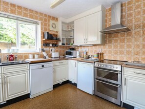 A kitchen with white cabinets, a dishwasher, a microwave, a stove, and a window with a view of greenery outside. - The Bungalow (Great Yarmouth)