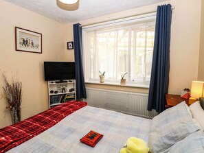 Ein Schlafzimmer mit einem Bett, einem Fernseher, einem Fenster mit Vorhängen, einer Heizung und einem Nachttisch mit einer Lampe.