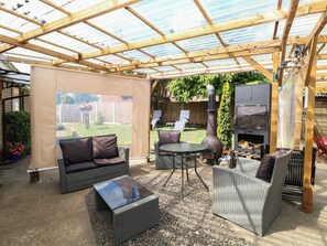 An outdoor patio area with wicker furniture, a glass-top table, and a barbecue grill. - The Bungalow (Great Yarmouth)