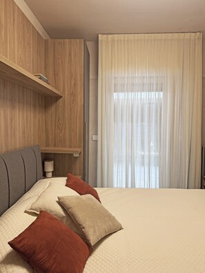 A hotel room with a bed, pillows, a bedside table, a lamp, and a window with curtains. - La Bauhaus by Wonderful Italy (Desenzano del Garda)