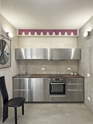 A compact kitchen with stainless steel appliances, a built-in oven, and a black chair. - La Bauhaus by Wonderful Italy (Desenzano del Garda)