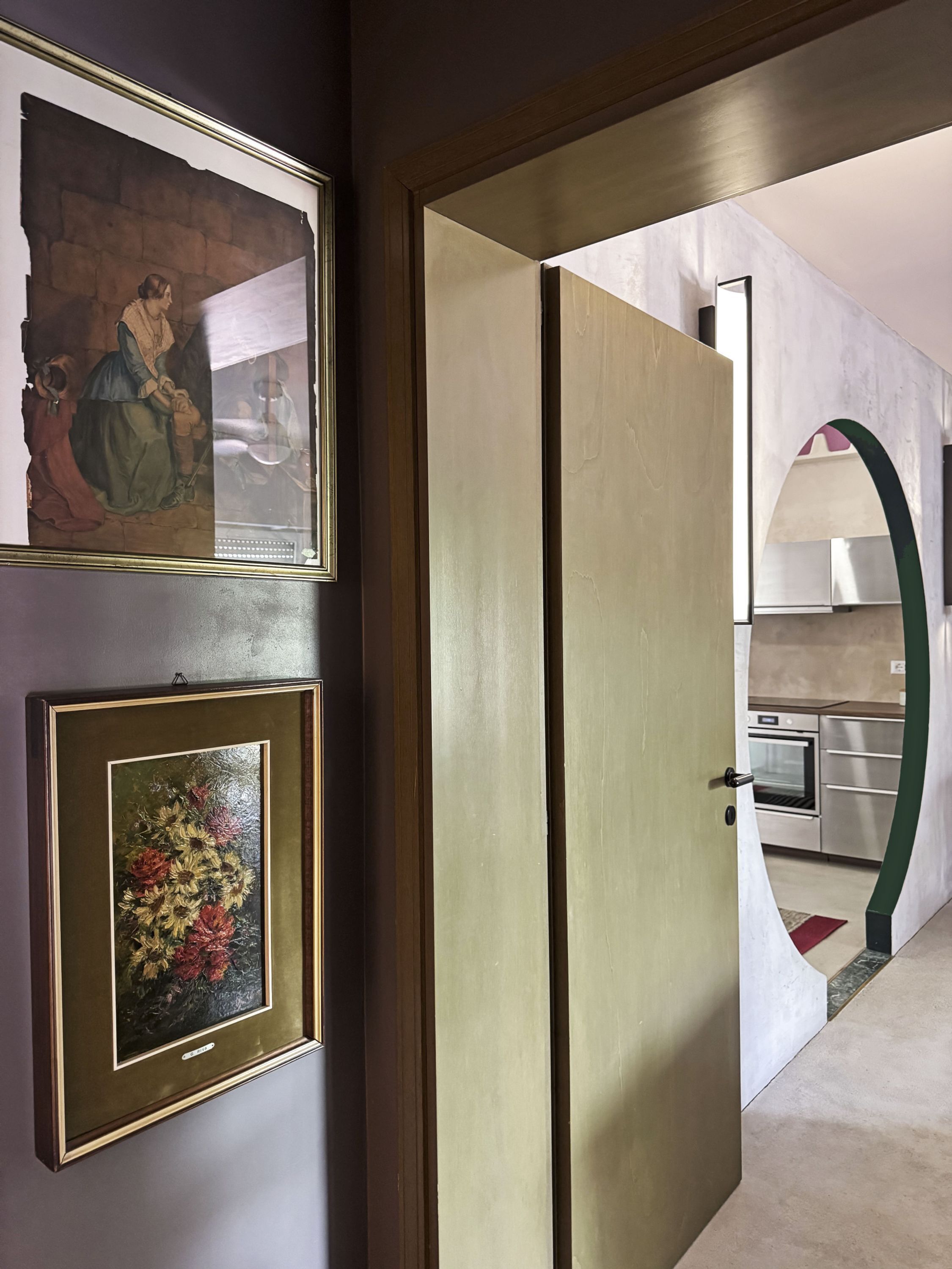 A hallway with a framed painting and a door leading to a kitchen area.
