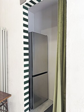 A corner of a room with a stainless steel refrigerator, a radiator, and a green curtain. - La Bauhaus by Wonderful Italy (Desenzano del Garda)
