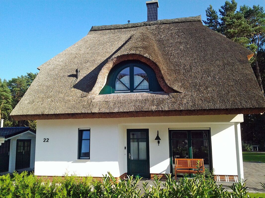 Une maison traditionnelle à toit de chaume, avec une porte verte, une petite fenêtre et le numéro « 22 » peint sur le mur.