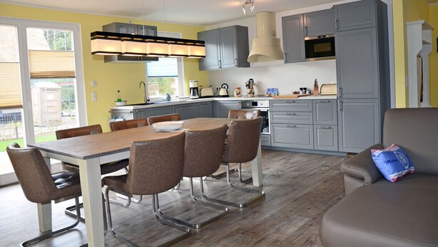 A modern kitchen with grey cabinets, a dining table with chairs, and a built-in oven. - Vacation home with a fireplace and sauna, about 300 meters from the sandy beach; pets welcome (Glowe)