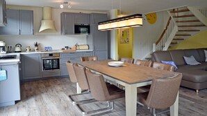 A modern kitchen with grey cabinets, a wooden dining table, and a staircase leading to a living area. - Vacation home with a fireplace and sauna, about 300 meters from the sandy beach; pets welcome (Glowe)