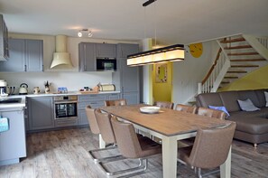 Eine moderne Küche mit grauen Schränken, einem Holztisch und einer Treppe, die in einen Wohnbereich führt.