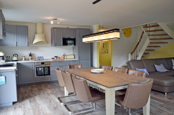 Une cuisine moderne avec des meubles gris, une table à manger en bois et un escalier menant à un espace de vie.