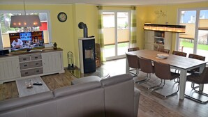 A modern kitchen with a dining area, a sofa, and a television displaying a cooking show. - Vacation home with a fireplace and sauna, about 300 meters from the sandy beach; pets welcome (Glowe)
