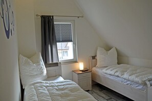 A room with two beds, a window with curtains, a nightstand with a lamp, and a wall with a simple design. - Vacation home with a fireplace and sauna, about 300 meters from the sandy beach; pets welcome (Glowe)