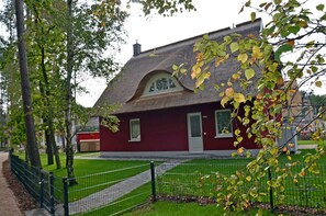 Ein rotes Gebäude mit einem geneigten Dach, einer kleinen Veranda und einem eingezäunten Garten.