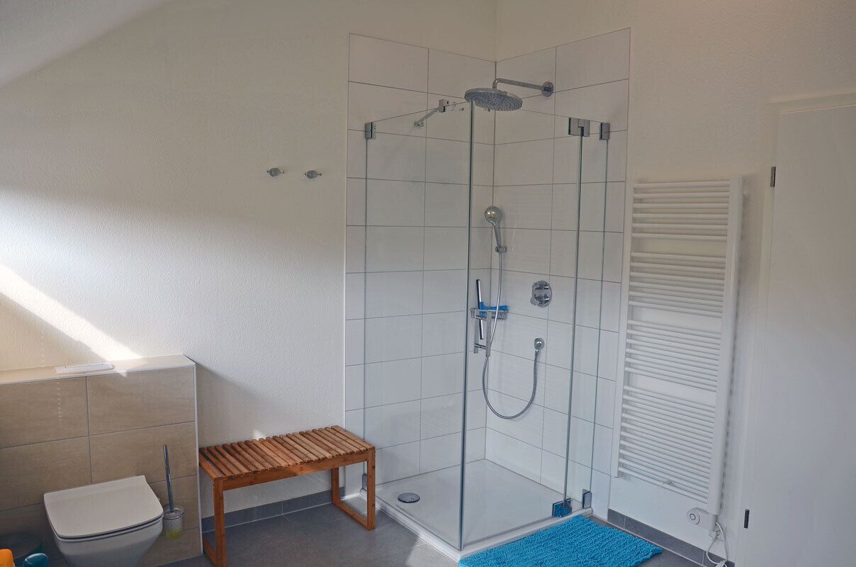 A shower area with a glass enclosure, a bench, and a white toilet.