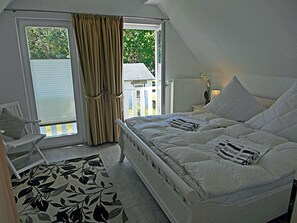 A bedroom with a bed, a chair, a window with curtains, and a view of the outside. - Vacation home with a fireplace, about 800 meters from the sandy beach, Wi-Fi, dogs welcome (Glowe)