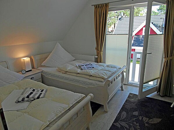 Une chambre avec deux lits, une table de chevet avec une lampe et une vue à travers une porte vitrée.