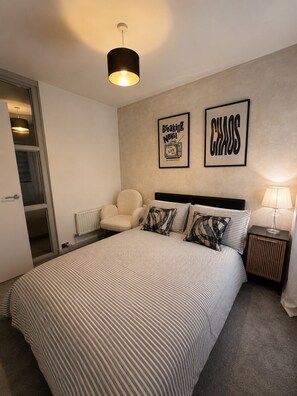A modern bedroom with a large bed, a chair, a nightstand, and two wall art pieces. - County Durham Home - Free Parking - 3 Bed (Chilton)