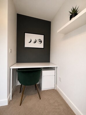 A corner room with a white desk, a green chair, a framed moon phase artwork, and a plant on a shelf. - County Durham Home - Free Parking - 3 Bed (Chilton)