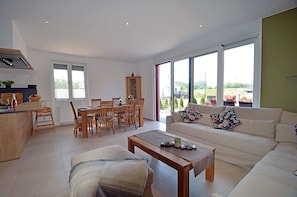A modern living room with a sofa, coffee table, and dining area with chairs and a cabinet.