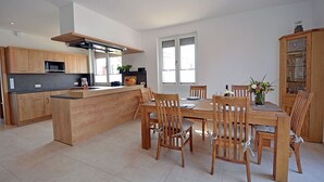 A modern kitchen with wooden cabinets, a central island, and a dining area with wooden chairs and a table.