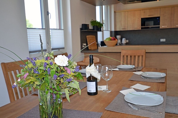 A dining table set for two with a bottle of wine, two wine glasses, and a vase of flowers.