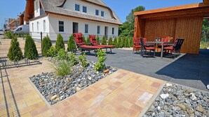 A house with a thatched roof, a patio with outdoor furniture, and a garden with small trees and a rock bed.