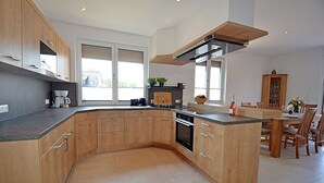 A modern kitchen with wooden cabinets, a built-in oven, and a dining area with a table and chairs.