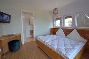 A bedroom with a wooden bed, a bedside table, a trash bin, a wardrobe, and a television.