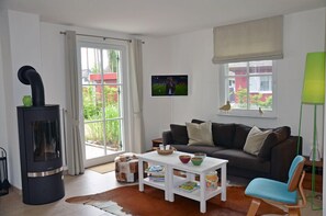 A living room with a sofa, a coffee table, a fireplace, and a window with a view of greenery. - Vacation home with a fireplace, about 300 meters from the sandy beach, 2 bedrooms, sleeps up to 4 people (Glowe)