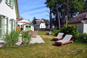 A courtyard with a thatched-roof house, a white house with green shutters, and two sun loungers. - Vacation home with a fireplace, about 300 meters from the sandy beach, 2 bedrooms, sleeps up to 4 people (Glowe)