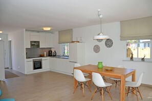 A modern kitchen with white cabinets, a wooden dining table, and white chairs. - Vacation home with a fireplace, about 300 meters from the sandy beach, 2 bedrooms, sleeps up to 4 people (Glowe)