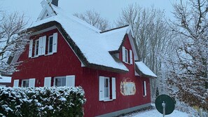 A red building with white shutters, a snow-covered roof, and a sign with a horse-drawn carriage illustration. - Vacation home with a fireplace and sauna, about 400 meters from the sandy beach, Wi-Fi, washing machine (Glowe)