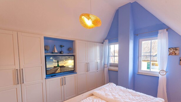 Une chambre à coucher comprenant un lit, un téléviseur fixé à un meuble, une fenêtre avec des rideaux et un luminaire au plafond.