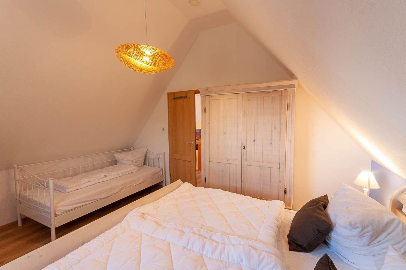 A bedroom with a bunk bed, a single bed, a wardrobe, and a hanging light fixture.