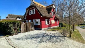 Ein rotes Haus mit einem Strohdach, einem gepflasterten Einfahrtsweg und einem Holzzaun.