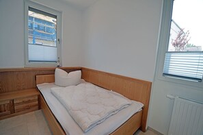 A bedroom with a wooden bed, a nightstand, a window with blinds, and a radiator. - 2-story vacation home, quiet location, about 1.3 kilometers from the sandy beach, Wi-Fi (Glowe)