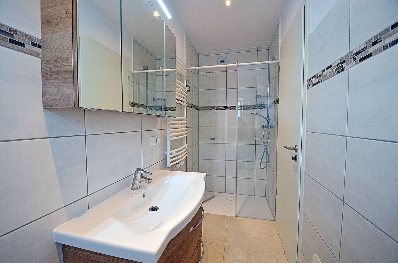 Een moderne badkamer met een wit wastafelmeubel, een glazen douchecabine en een houten kast.