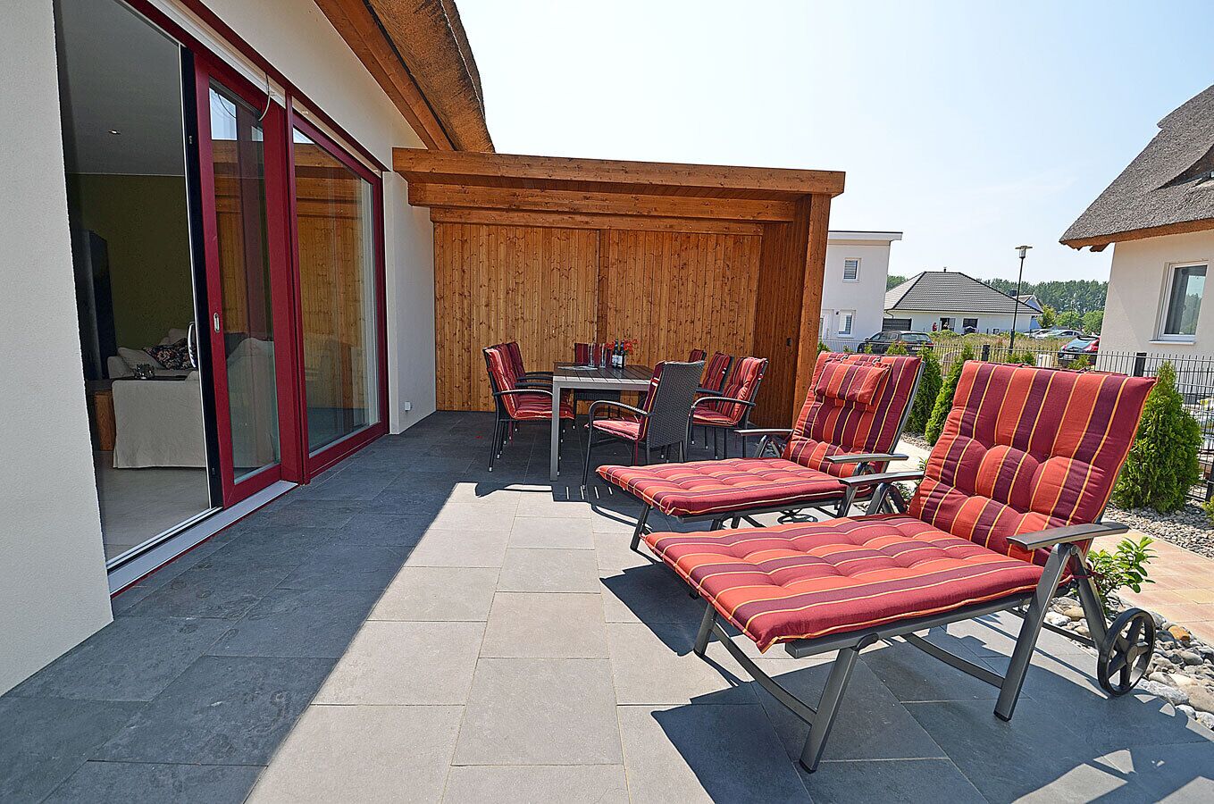 En udendørs terrasse med spisebord, stole og liggestole.