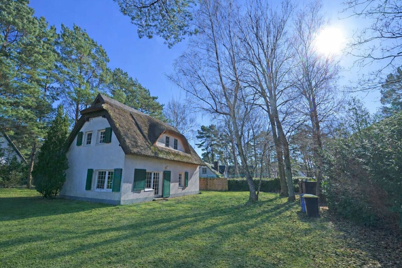 Een traditioneel huis met rieten dak, omringd door bomen en een verzorgd gazon.