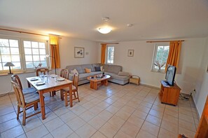 A living room with a dining table, two sofas, a TV stand, and a window with curtains. - Vacation home with a sauna, about 300 meters from the sandy beach, Wi-Fi, and a washing machine (Glowe)