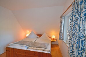 A bedroom with a bed, bedside lamps, a window with patterned curtains, and a wooden dresser. - Vacation home with a sauna, about 300 meters from the sandy beach, Wi-Fi, and a washing machine (Glowe)