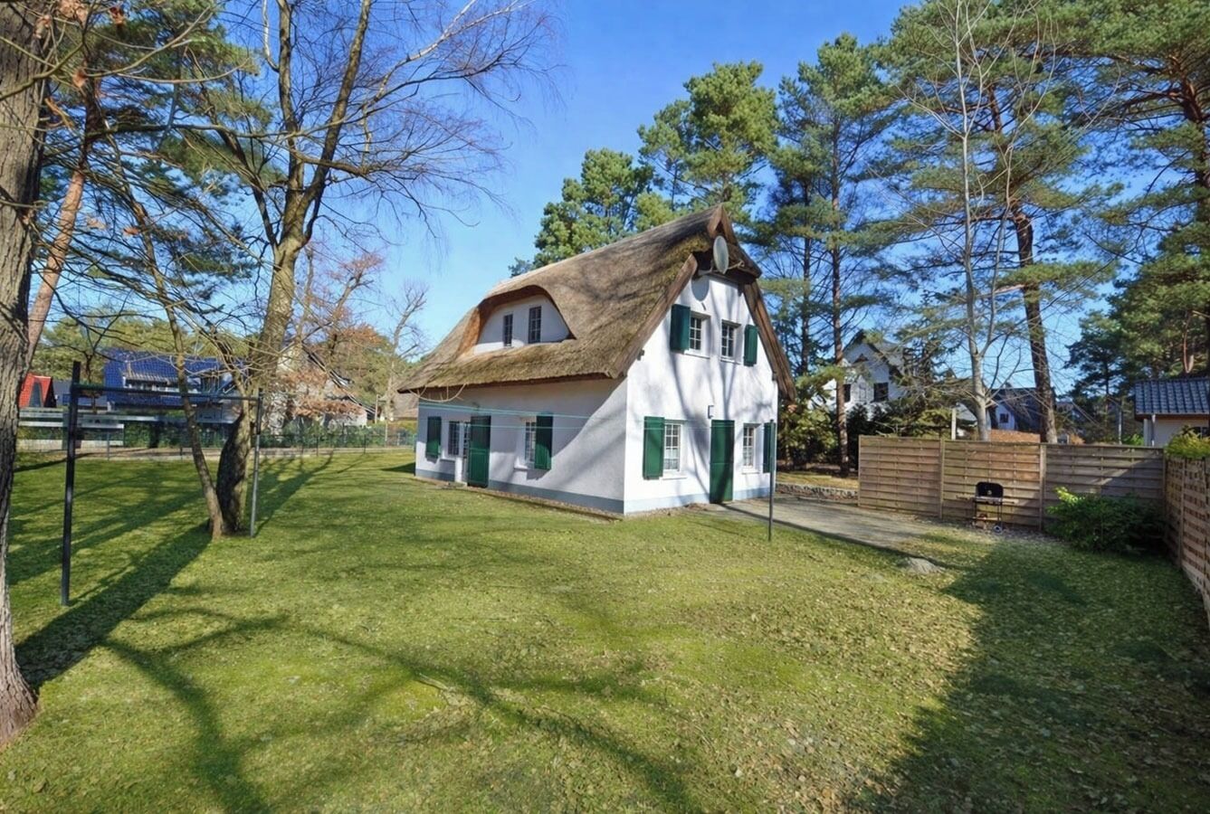 A traditional house with a thatched roof, surrounded by a well-maintained lawn and trees.