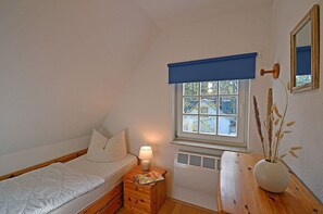 A bedroom with a single bed, a bedside table with a lamp, a window with a view of trees, and a wall-mounted mirror. - Vacation home with a sauna, about 300 meters from the sandy beach, Wi-Fi, and a washing machine (Glowe)