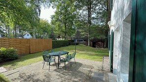 A patio with a table and chairs, surrounded by a wooden fence and greenery. - Vacation home with a sauna, about 300 meters from the sandy beach, Wi-Fi, and a washing machine (Glowe)